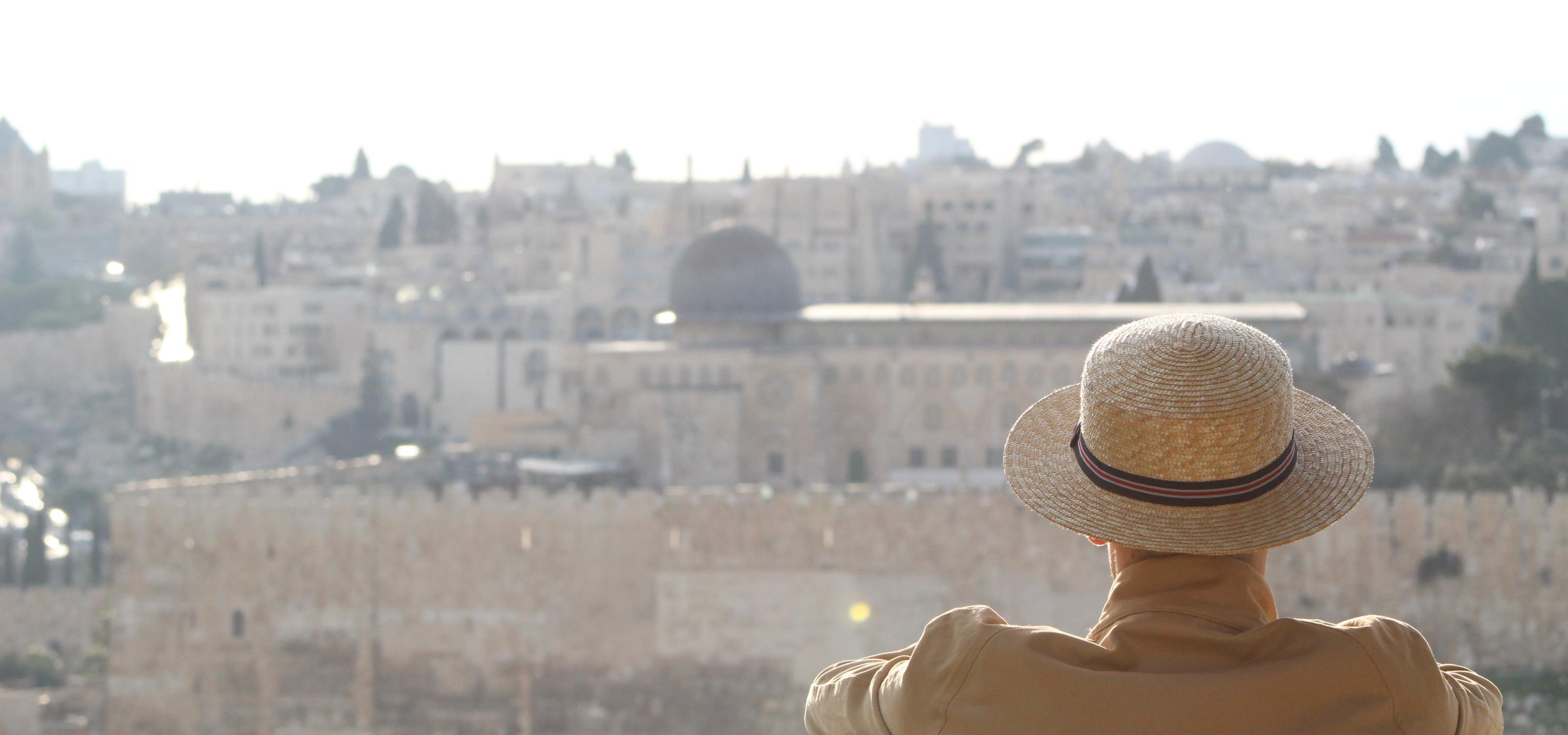 A man sits, back to the camera, with the Old City and al-Aqsa mosque visible in the background.