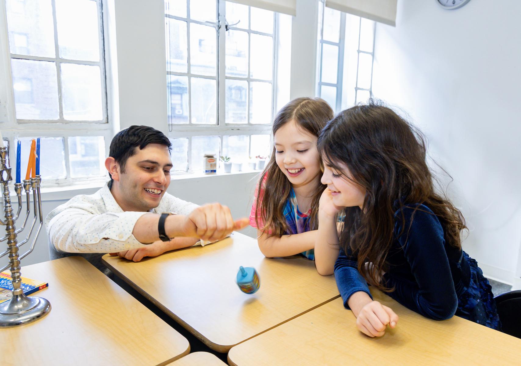 Educator and upper-elementary kids spinning a dreidel 