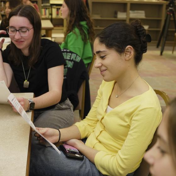 Students sit at tables and read from printed text sheets