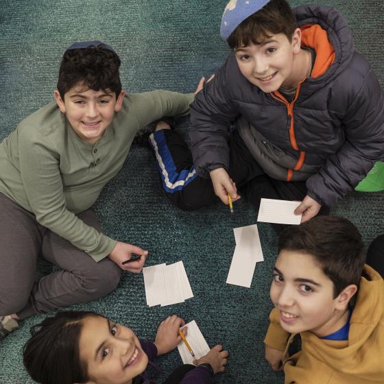 Four students sit on the floor with pencils and notecards