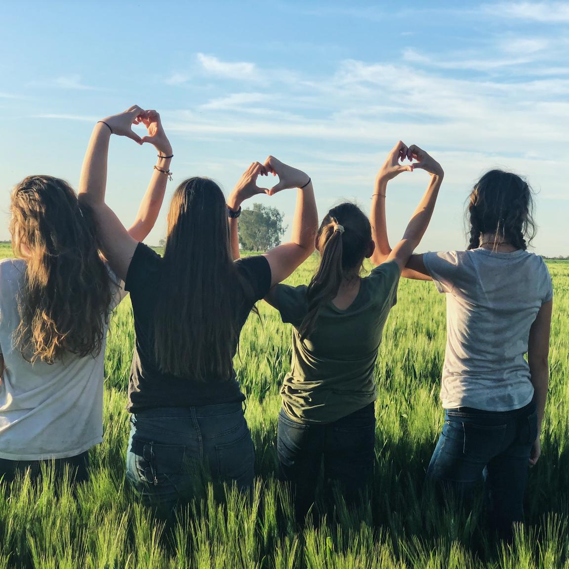 Four children sit in a field with their back to the camera, making hearts with their hands together. 
