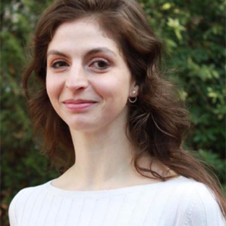 Loen stands in front of a leafy background, wearing a white shirt and smiling.
