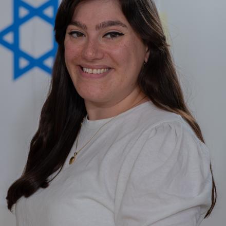 A headshot of May Brown in front of an Israeli flag. 