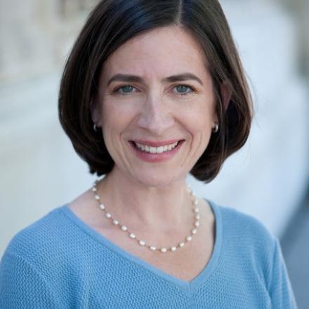 A headshot of Deborah Shapira in front of a stone wall. 