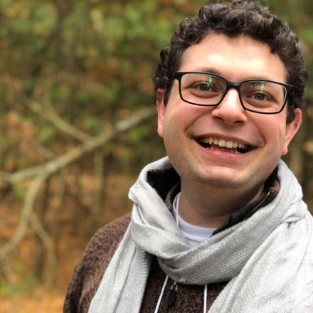 A headshot of Amram in front of a wooded background.