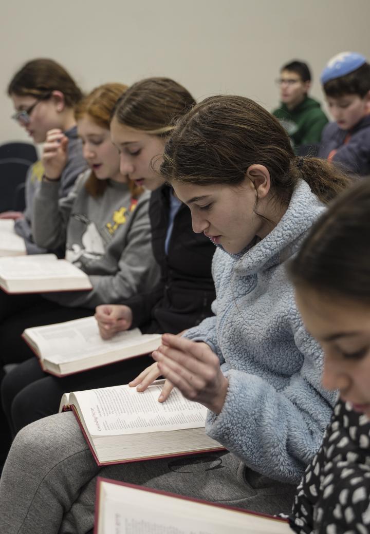 children in rows reading from primary text