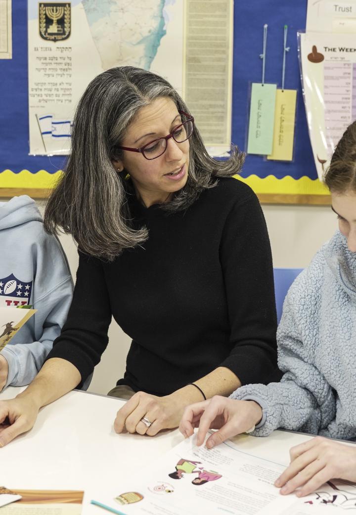 one educator and two learners sit at a table, looking through multiple text sources